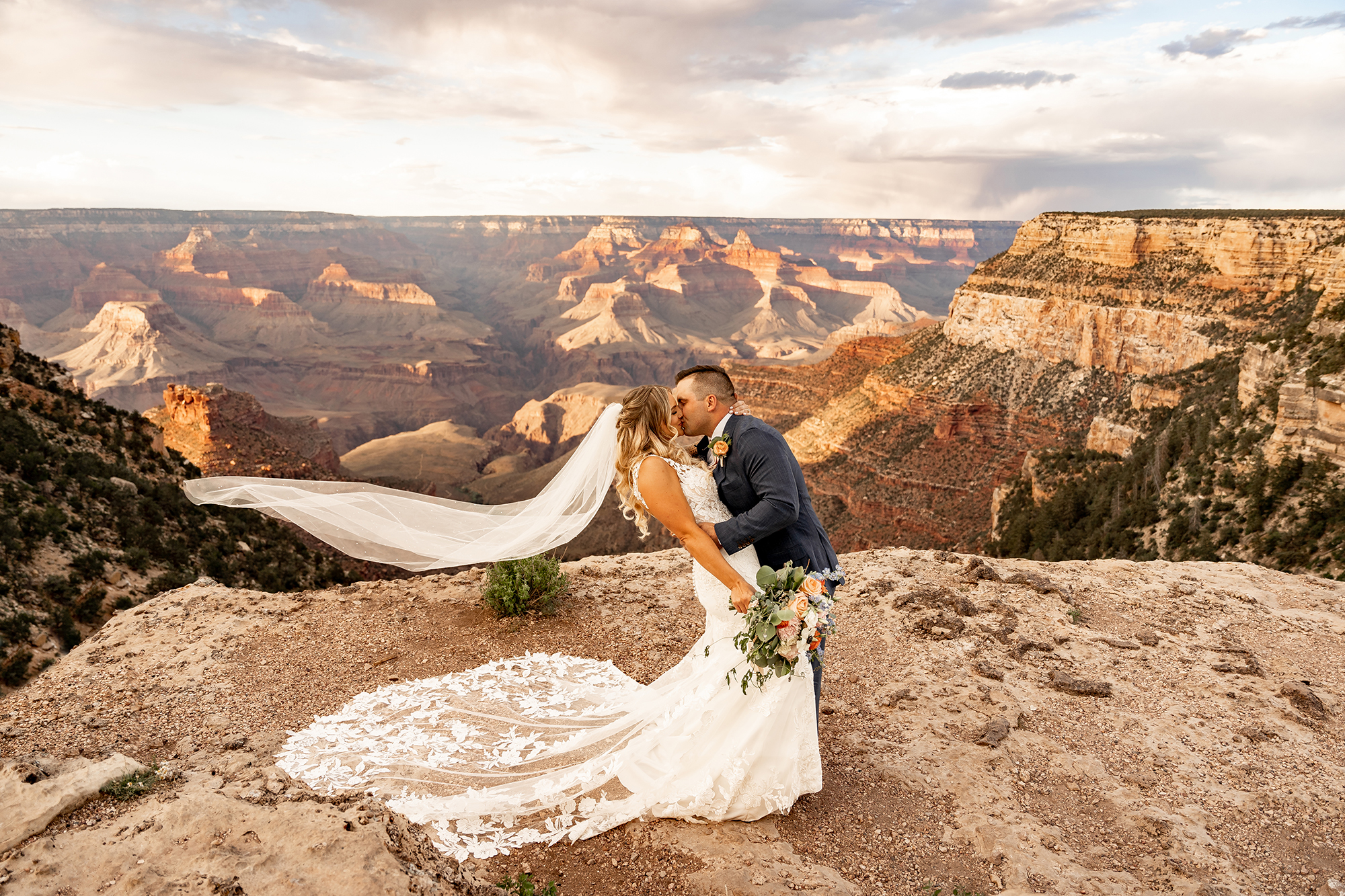 bride and groom kissing on the south rim of the grand canyon. her veil is flowing in the wind.